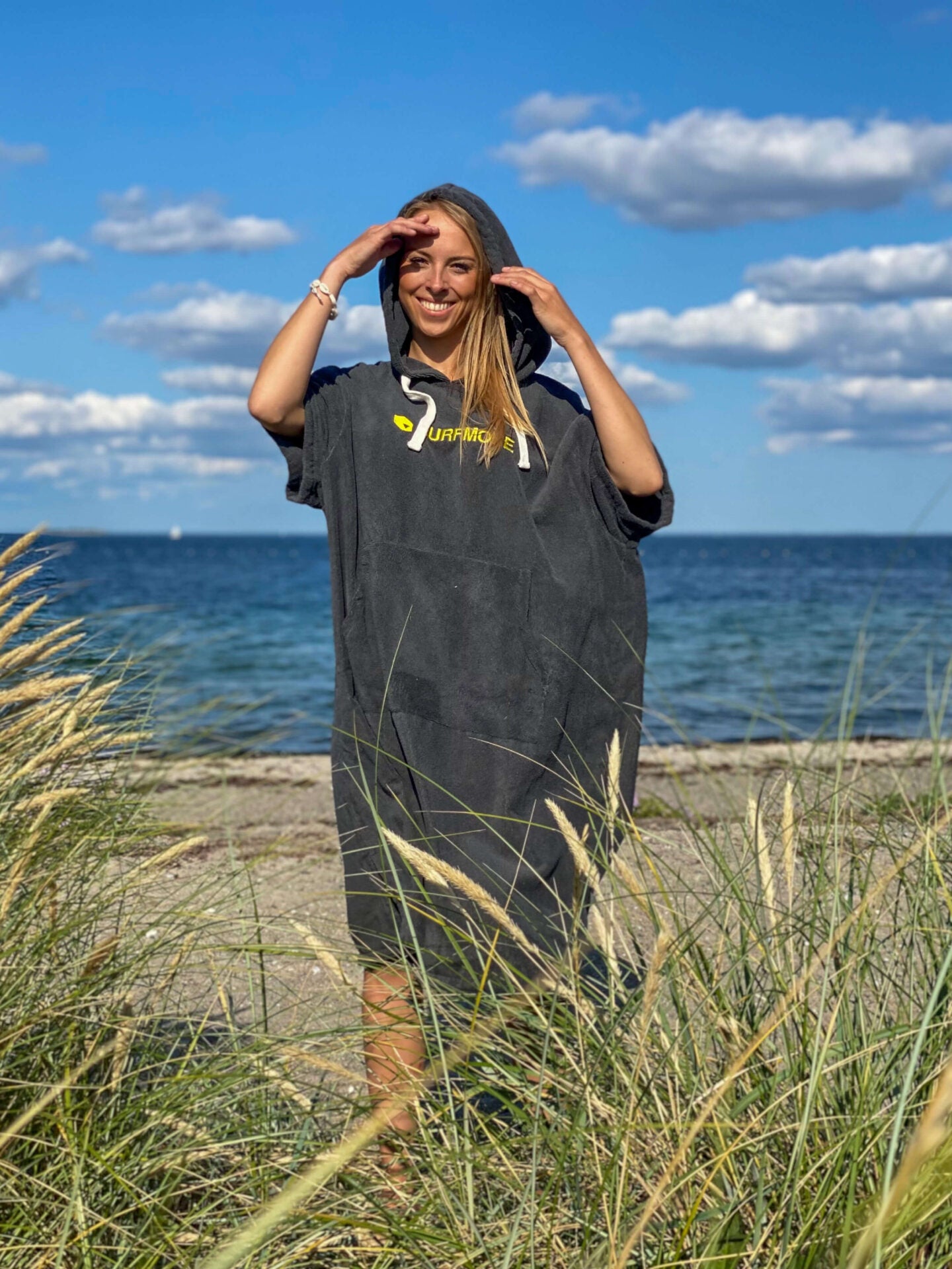 Ung og smilende dame med lyst hår står i en badeponcho i grå